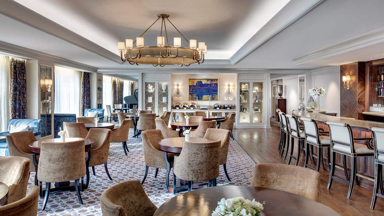 Elegant dining area with round tables, cushioned chairs, a chandelier, and a bar counter with high stools.