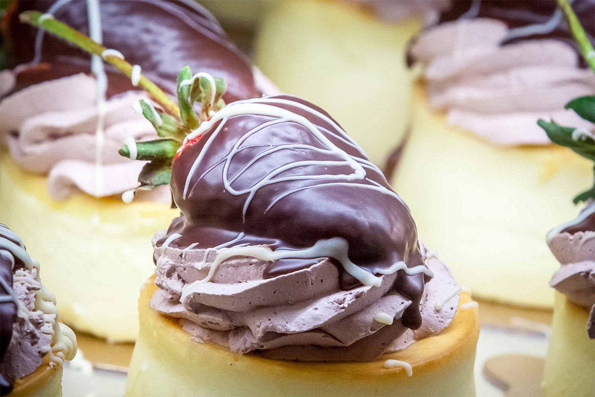 Chocolate-covered strawberries on top of cream-topped cheesecake with a white chocolate drizzle.