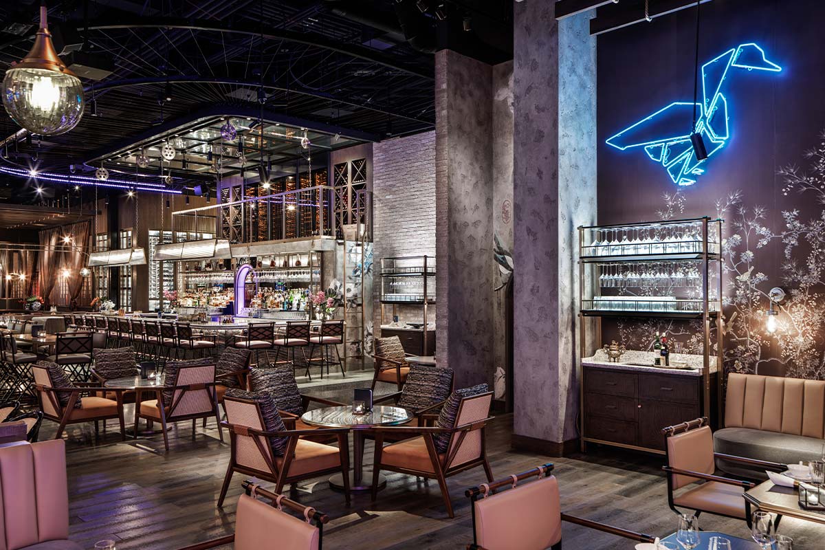 Modern bar interior with cozy seating, illuminated neon bird decoration on the wall, and well-lit bar counter in the background.