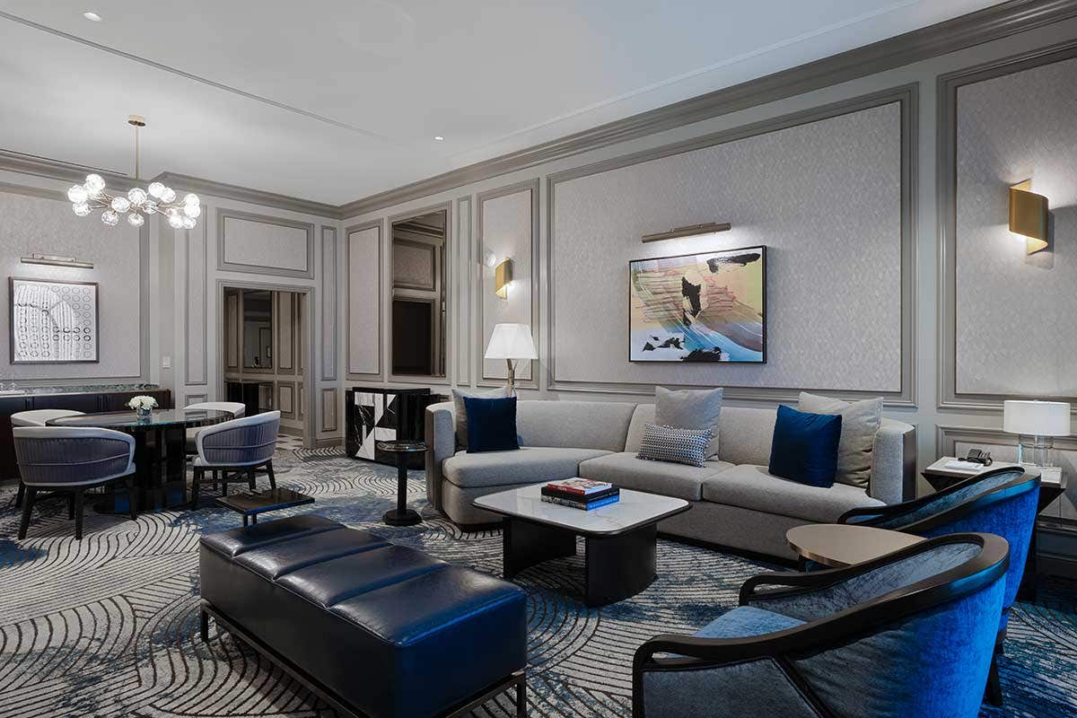 Modern living room with gray sectional sofa, abstract art, blue accents, and spherical chandelier.