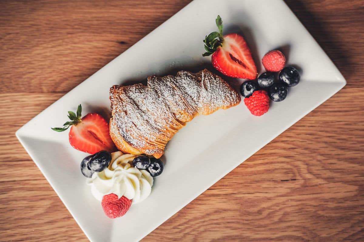 Croissant with powdered sugar, strawberries, blueberries, raspberries, and whipped cream on a white plate.