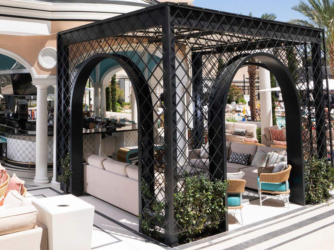 Luxurious outdoor lounge area with modern seating and lattice structure, with tall buildings in the background.