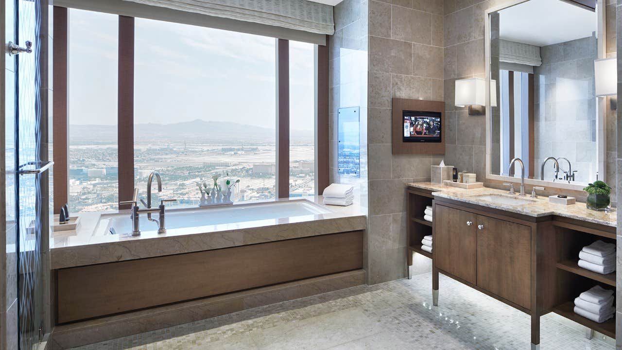 Luxurious bathroom with a large window offering a scenic view, a bathtub, a double sink, and a wall-mounted TV.