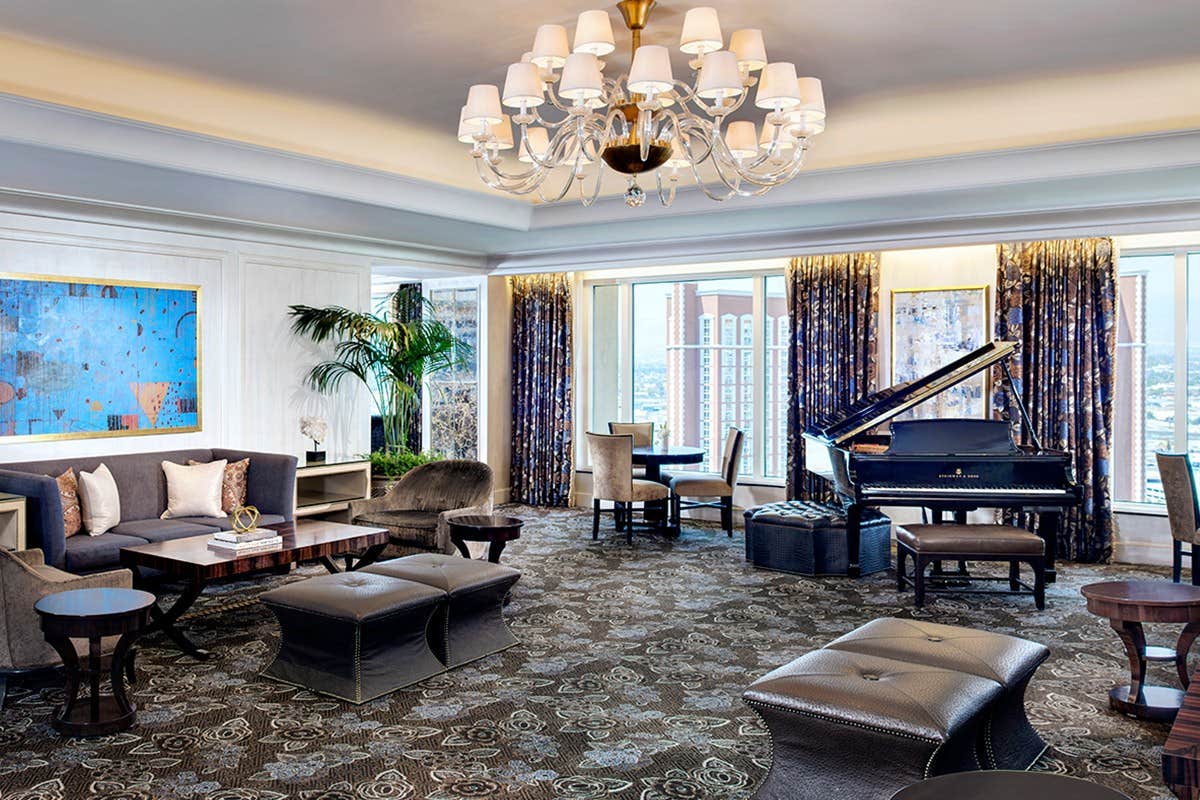 Luxurious living room with elegant furniture, chandelier, art pieces, grand piano, large windows with city views.