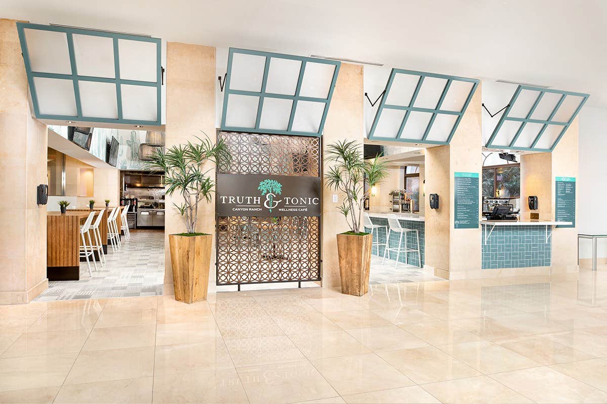 Cafe entrance with "Truth & Tonic" sign, glass windows, modern decor, potted plants, and seating area inside.