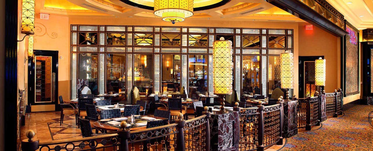 Elegant restaurant with warm lighting, ornate decor, and neatly set tables, enclosed by decorative railings.