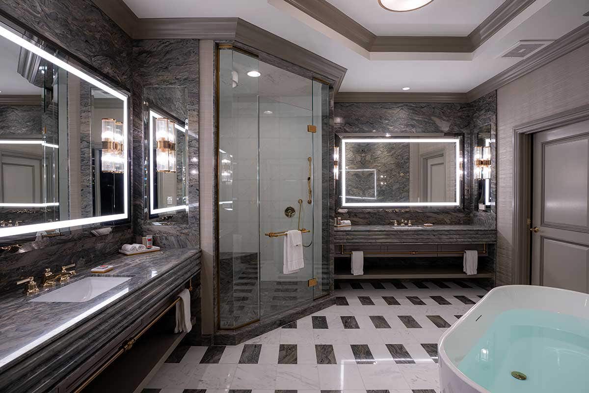 Luxurious bathroom with marble surfaces, illuminated mirrors, a glass-enclosed shower, and a large bathtub.