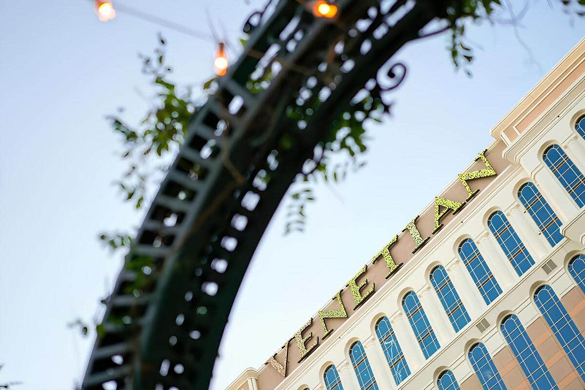 View of a building with "Venetian" sign, seen through an archway with lights and greenery.