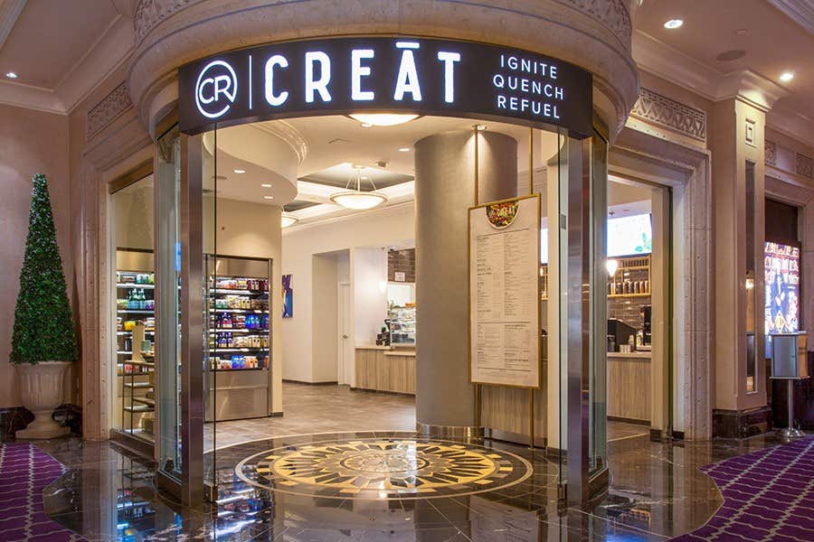 Entrance to a modern cafe named CREAT, featuring a circular floor design and displaying snacks and menus.