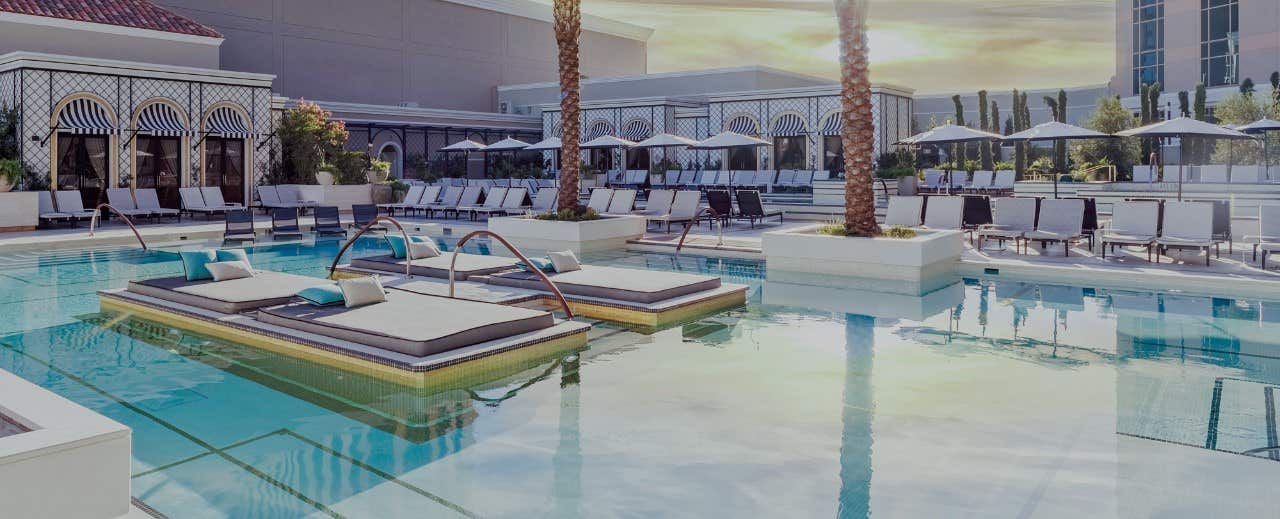 Luxurious outdoor pool area with lounge chairs, umbrellas, palm trees, and floating sunbeds, set against elegant architecture.