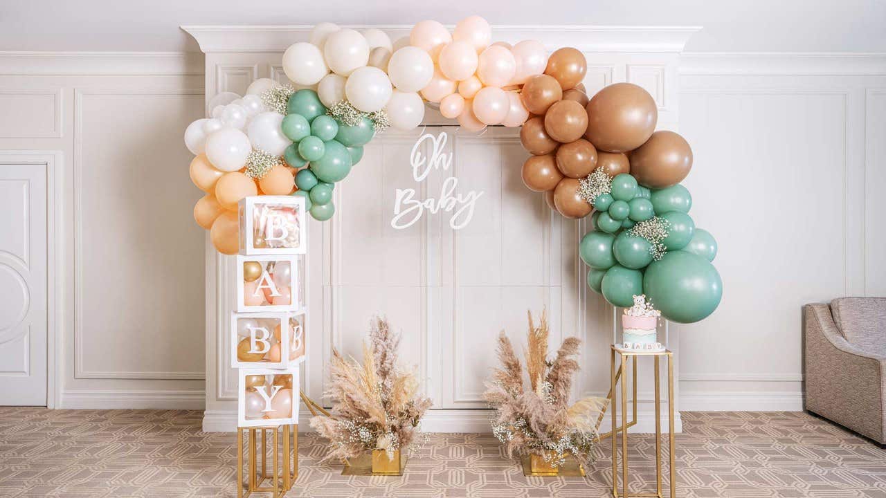 A balloon arch with pastel colors, "Oh Baby" sign, BABY blocks, pampas grass, and a small cake on a stand.