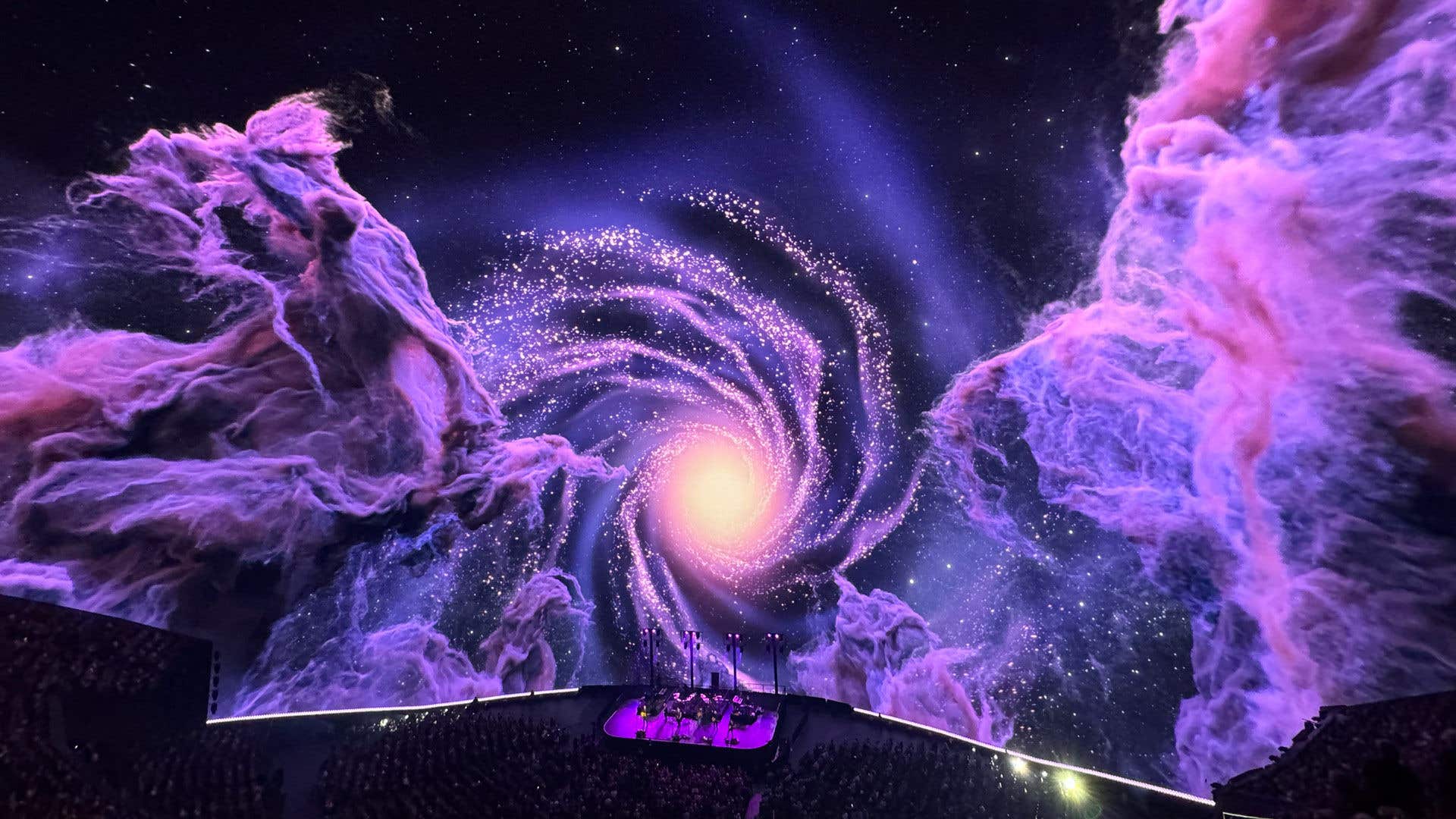 A dramatic view of a spiral galaxy and nebulae on a theater screen, with an audience in the foreground.