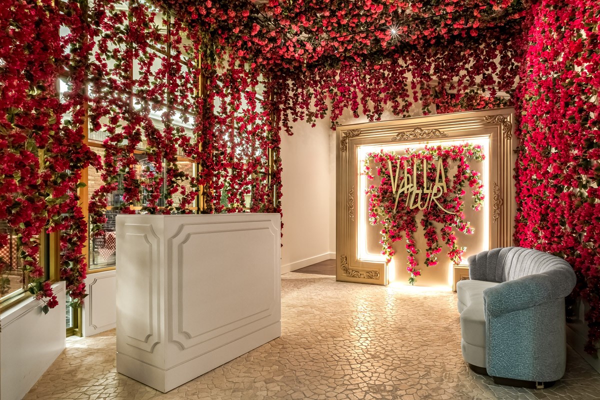 Luxurious interior with walls and ceiling covered in red flowers, a white reception desk, and an ornate gold-framed sign.