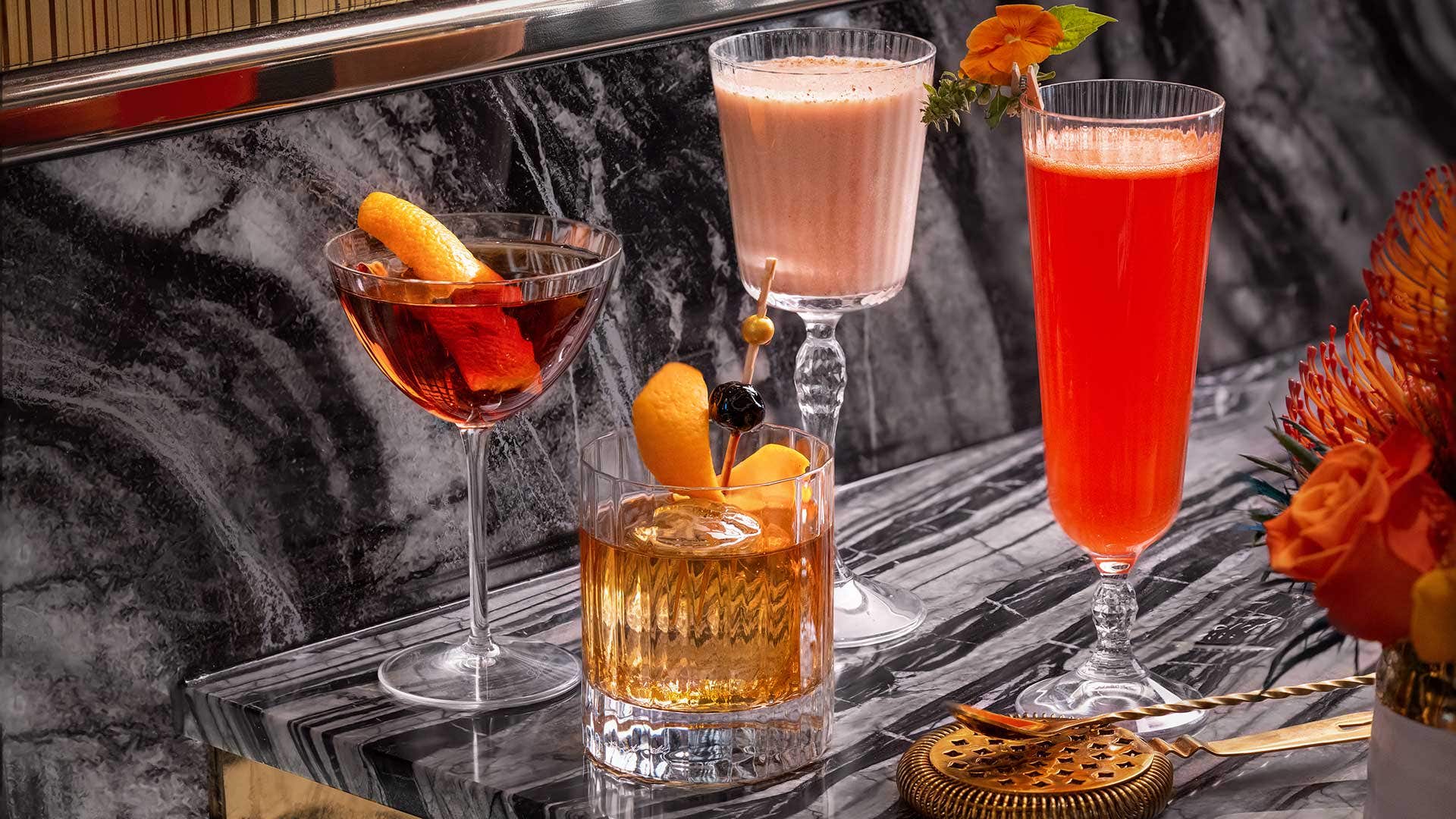 Four cocktails in different glasses on a grey table.