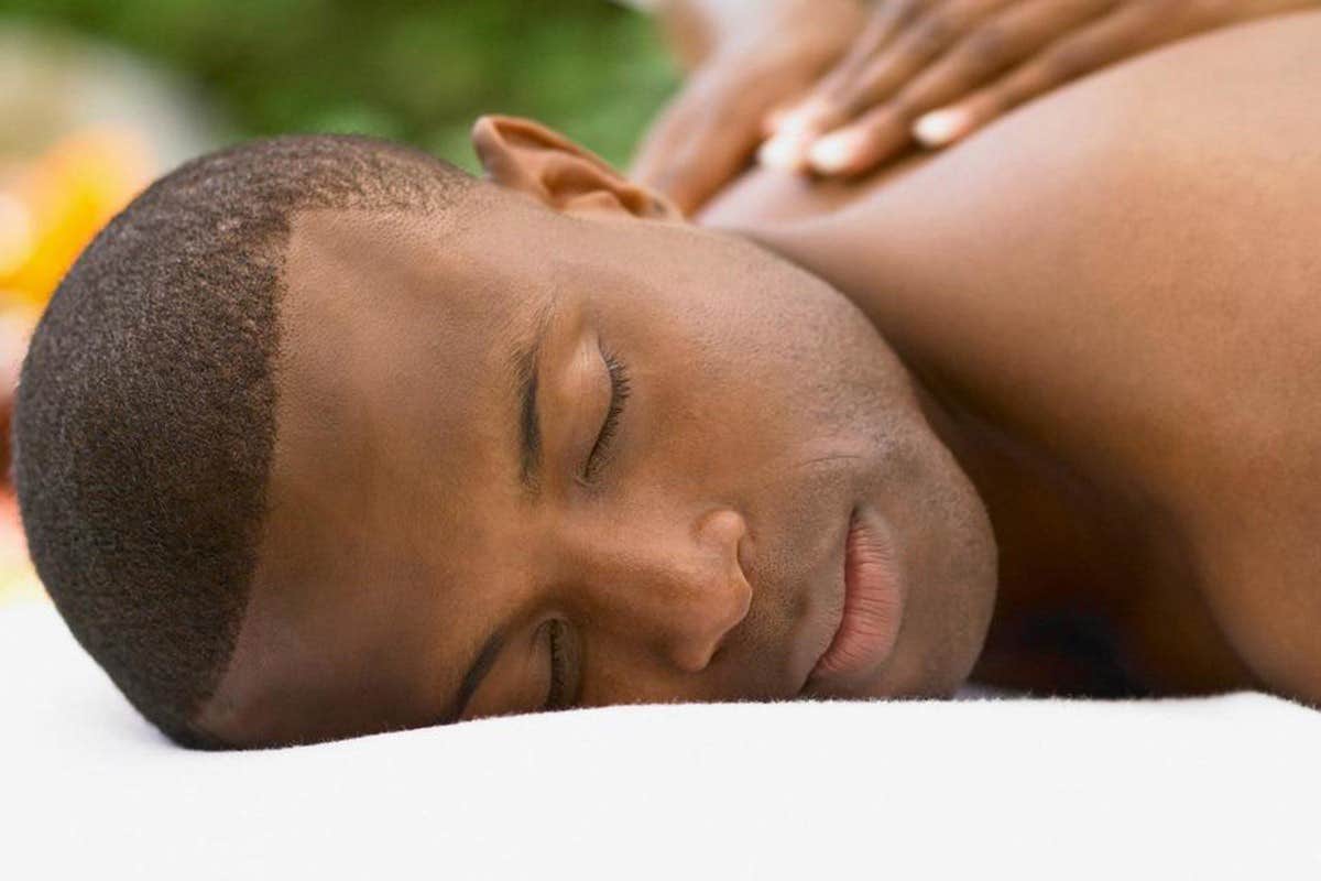 A person with short hair lying face down on a massage table, receiving a relaxing back massage.