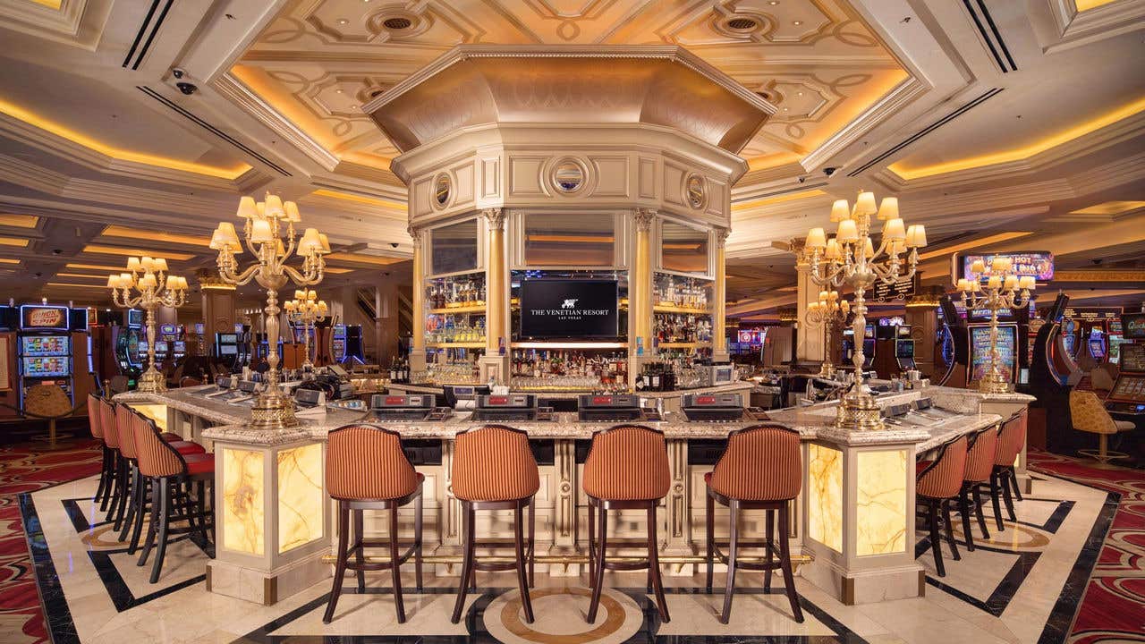 Bellini Bar with marble top, surrounded by plush barstools, chandeliers, and slot machines in the background.