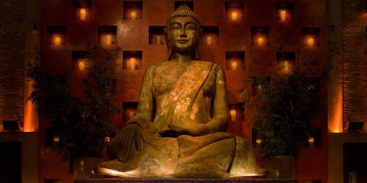 A large Buddha statue in a dimly lit restaurant with candles and bamboo plants surrounding it.