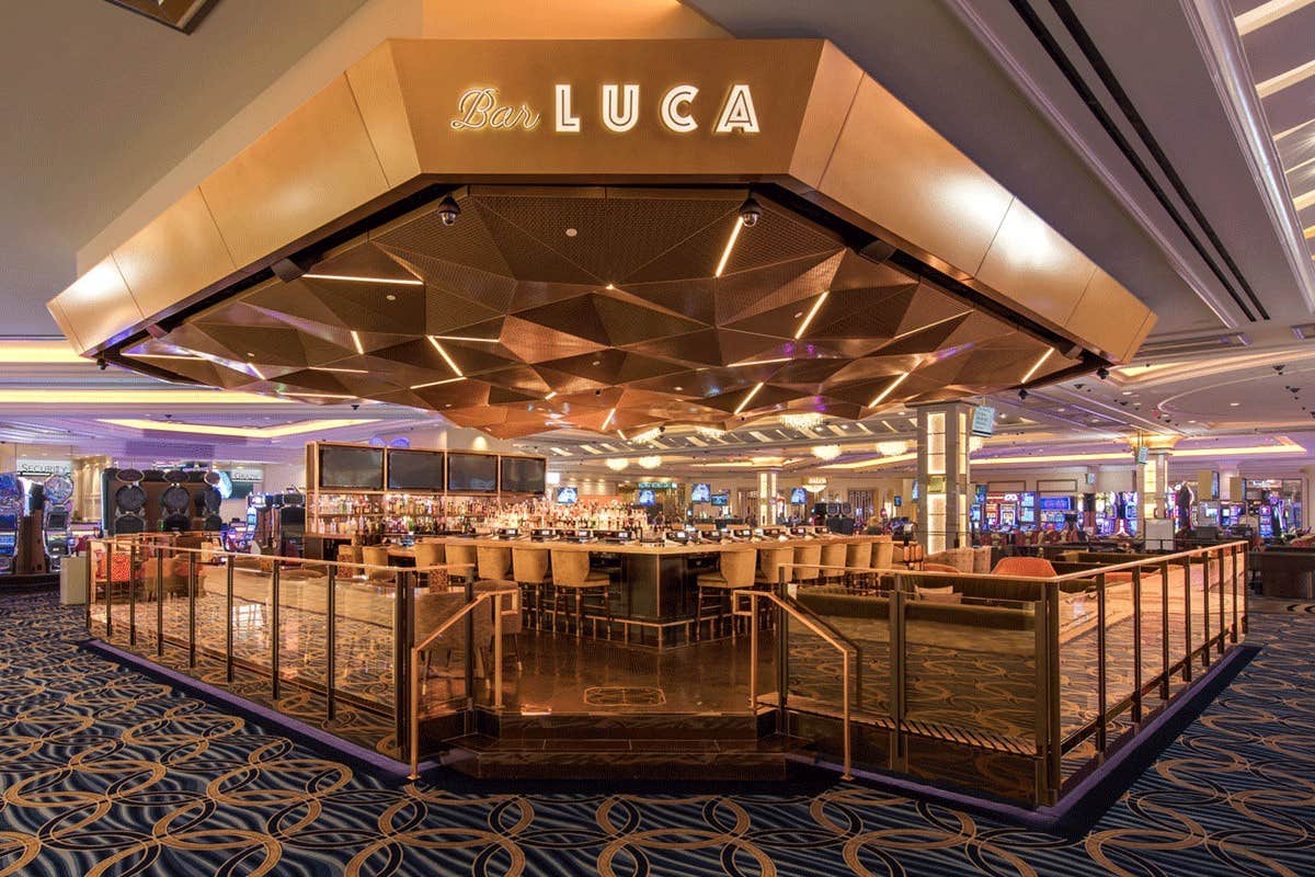 An upscale bar named "Bar LUCA" with modern decor, central bar seating, and a geometric ceiling in a large casino.