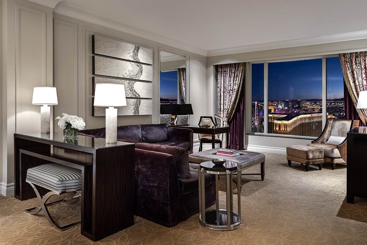 Luxurious hotel suite with elegant furniture, night city view through large windows, and warm ambient lighting.