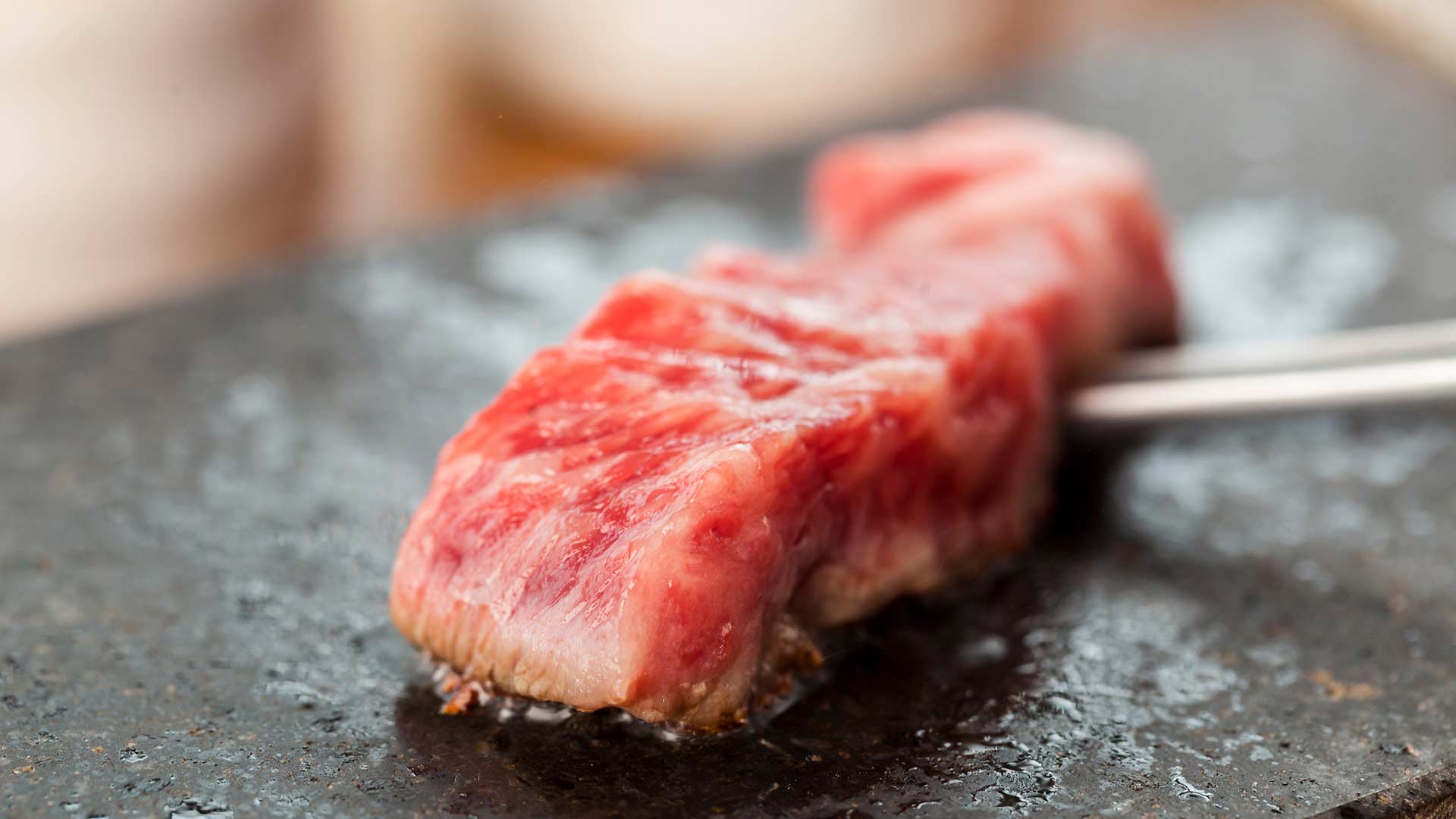 Close-up of raw marbled beef being cooked on a hot surface with tongs.