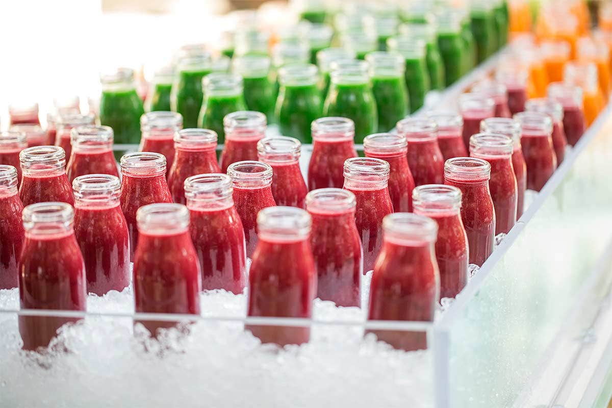 Rows of glass bottles filled with red and green smoothies, displayed on ice in a clean, organized setup.