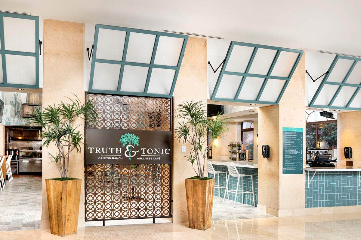 Entrance to Truth & Tonic wellness café with plants in large planters, a counter, and a menu board on the right.