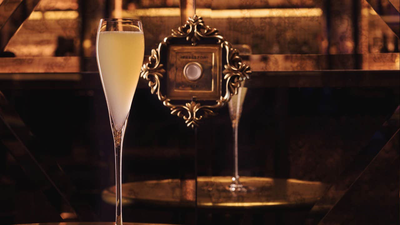 A glass of champagne on a gold table with an ornate, reflective background.