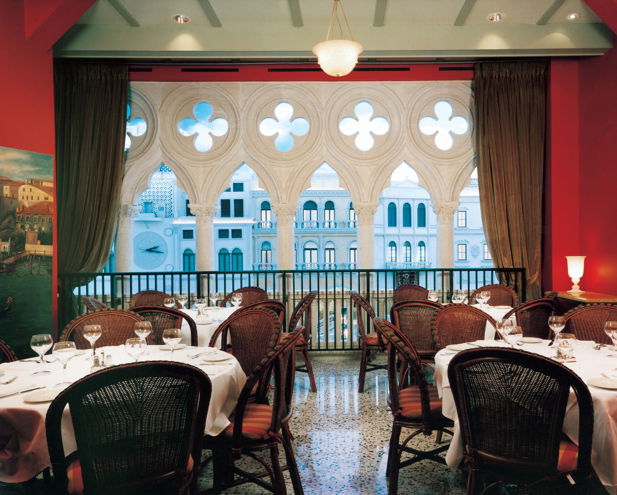 Elegant restaurant with a Venetian-themed decor, featuring arched windows overlooking a balcony and neatly set tables.