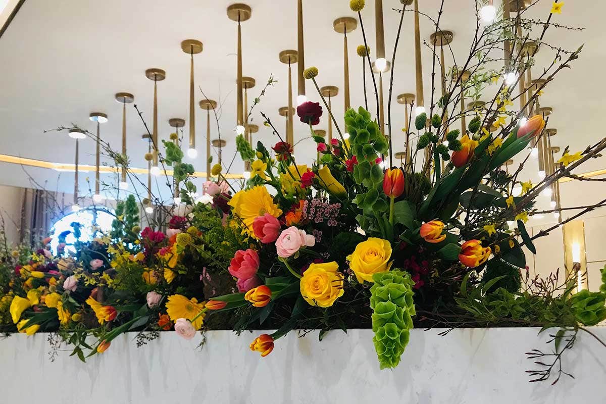 An arrangement of colorful flowers in a modern space with gold pendant lights in the background.