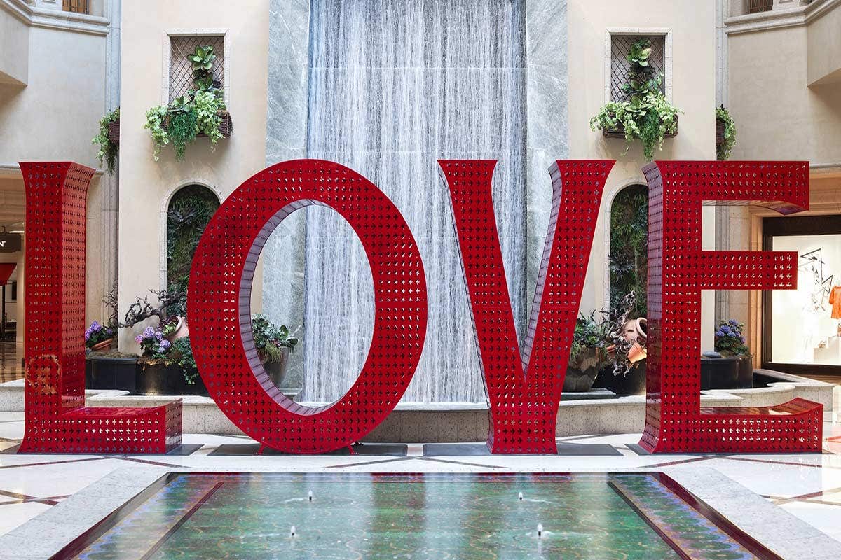 Large red "LOVE" sculpture in front of an indoor waterfall, surrounded by plants and greenery.