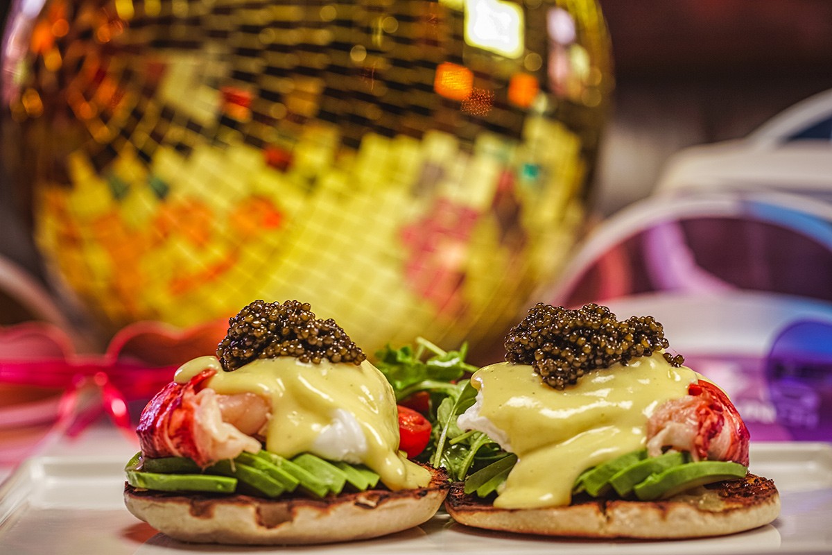 Gourmet eggs Benedict topped with caviar on a reflective surface with a gold disco ball in the background.