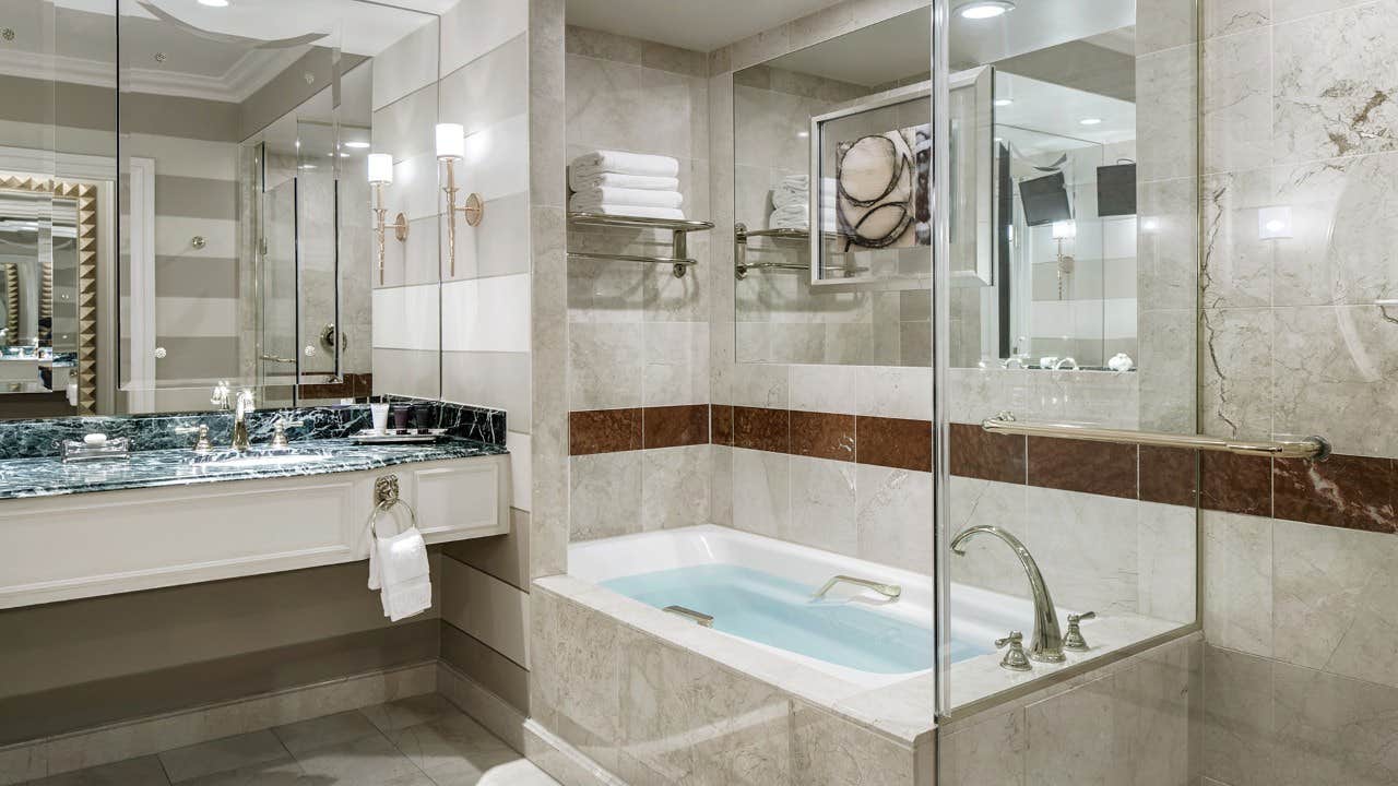 Luxurious bathroom with a bathtub, glass shower, granite countertop, large mirror, and elegant lighting fixtures.