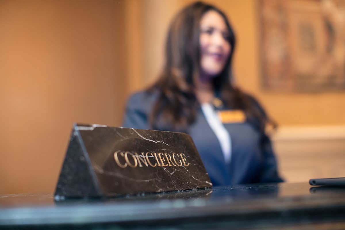 Close-up of a concierge sign on a counter with a blurred woman wearing a suit in the background.