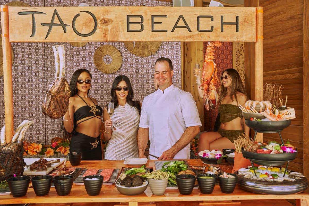 Four people at a food stall labeled "TAO BEACH," displaying various food items.