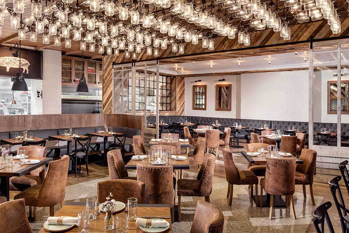 A modern, cozy restaurant with wooden decor, leather chairs, and elegant lighting, neatly set tables ready for diners.