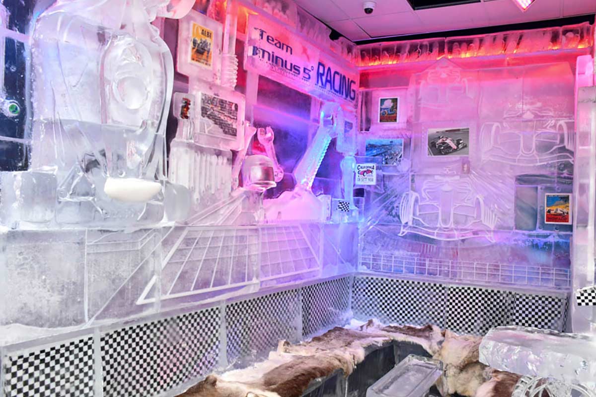 A room with walls, furniture, and decor made entirely of ice, featuring racing-themed decorations and neon lights.