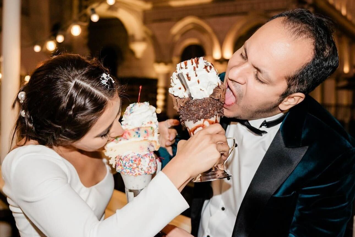 A newly married couple taking bites of giant ice cream cones at Black Tap