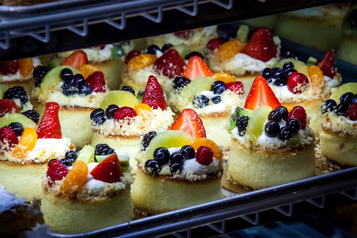 Freshly baked mini cheesecakes topped with assorted fruits displayed on a metal rack.