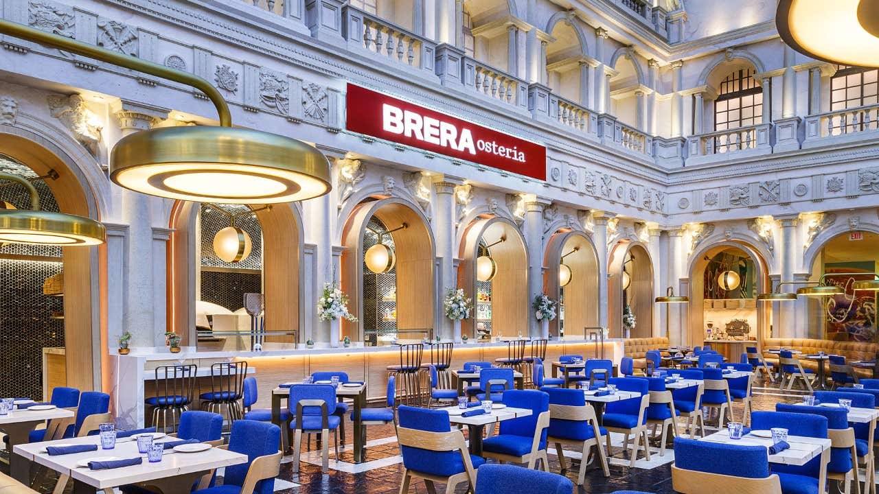 Elegant restaurant interior with blue and white seating, under high ceilings, with a sign reading "BRERA osteria".