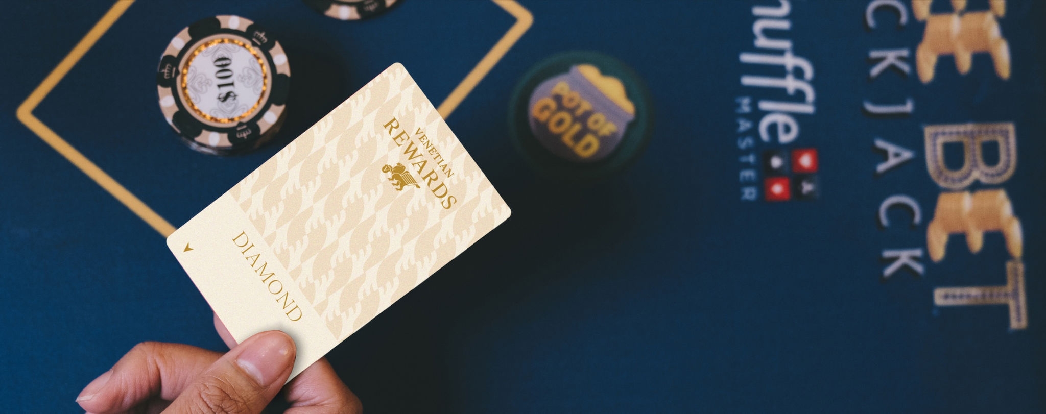 Hand holding a "Diamond" rewards card over a blackjack table with poker chips and a cup labeled "Pot of Gold.