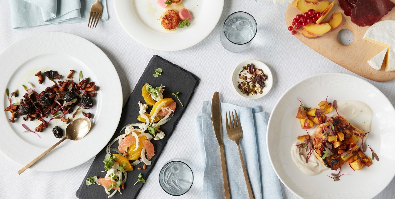 A table set with assorted gourmet dishes, cutlery, and glasses of water on a white tablecloth.