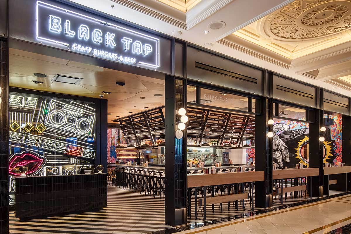 Modern fast-food restaurant with a neon sign, featuring an open kitchen, bar seating, and vibrant wall art.