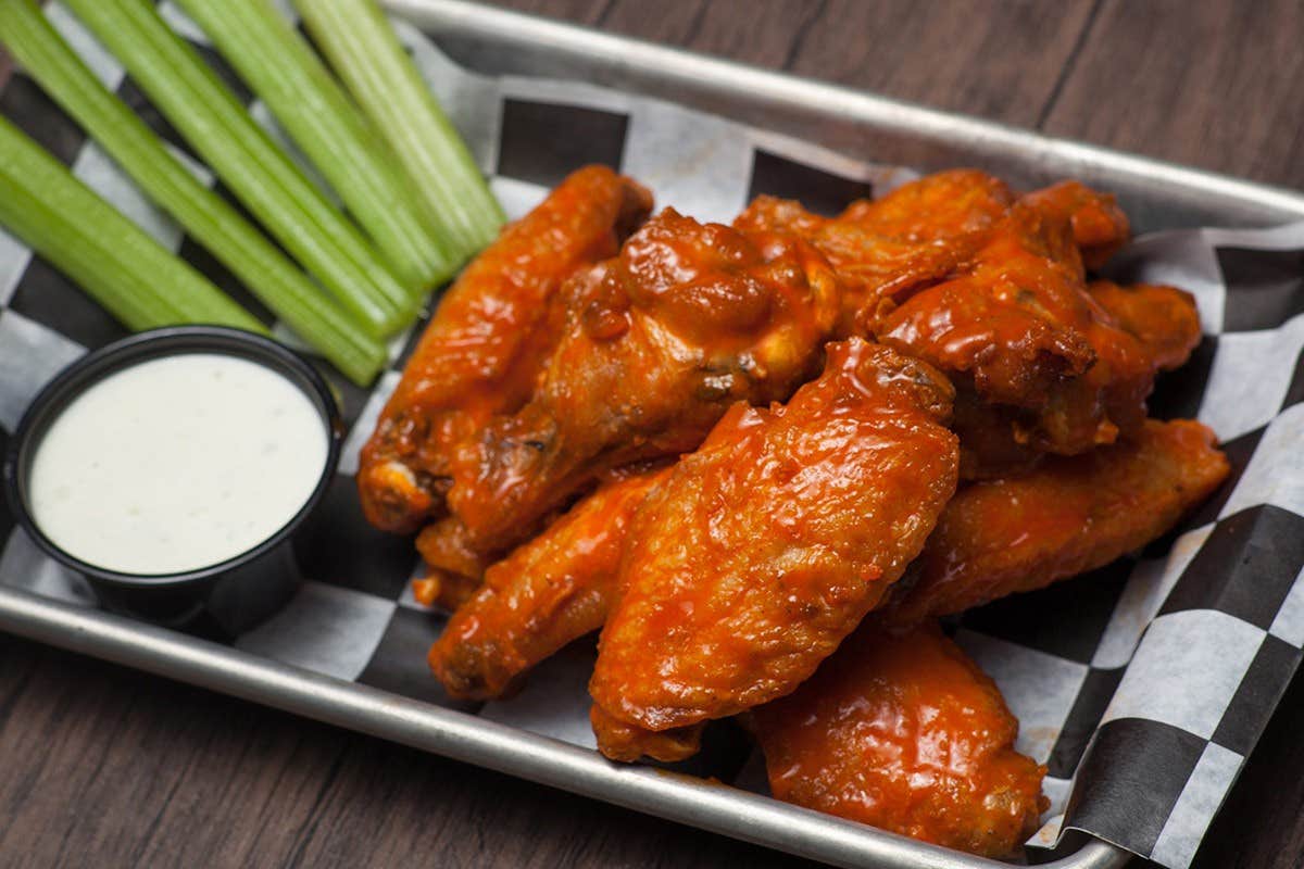 Buffalo chicken wings with a side of celery sticks and a cup of ranch dipping sauce on a tray.