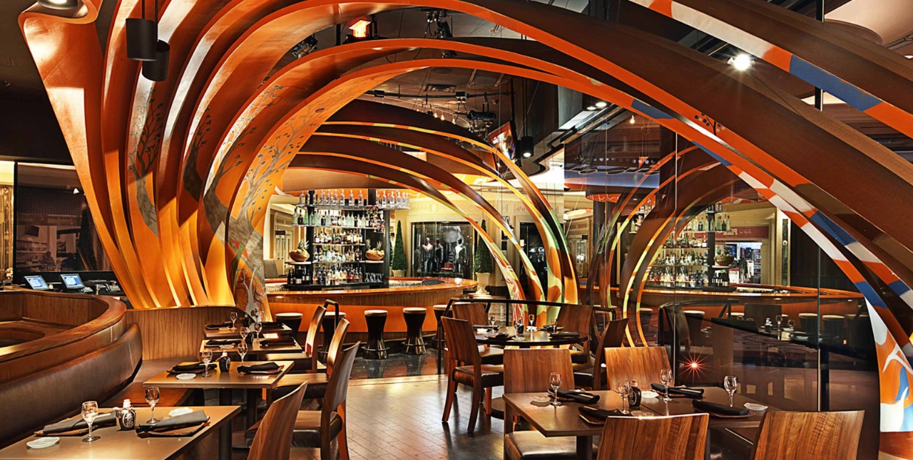 A modern restaurant interior with wooden tables, chairs, and unique curved orange ceiling beams creating an artistic atmosphere.