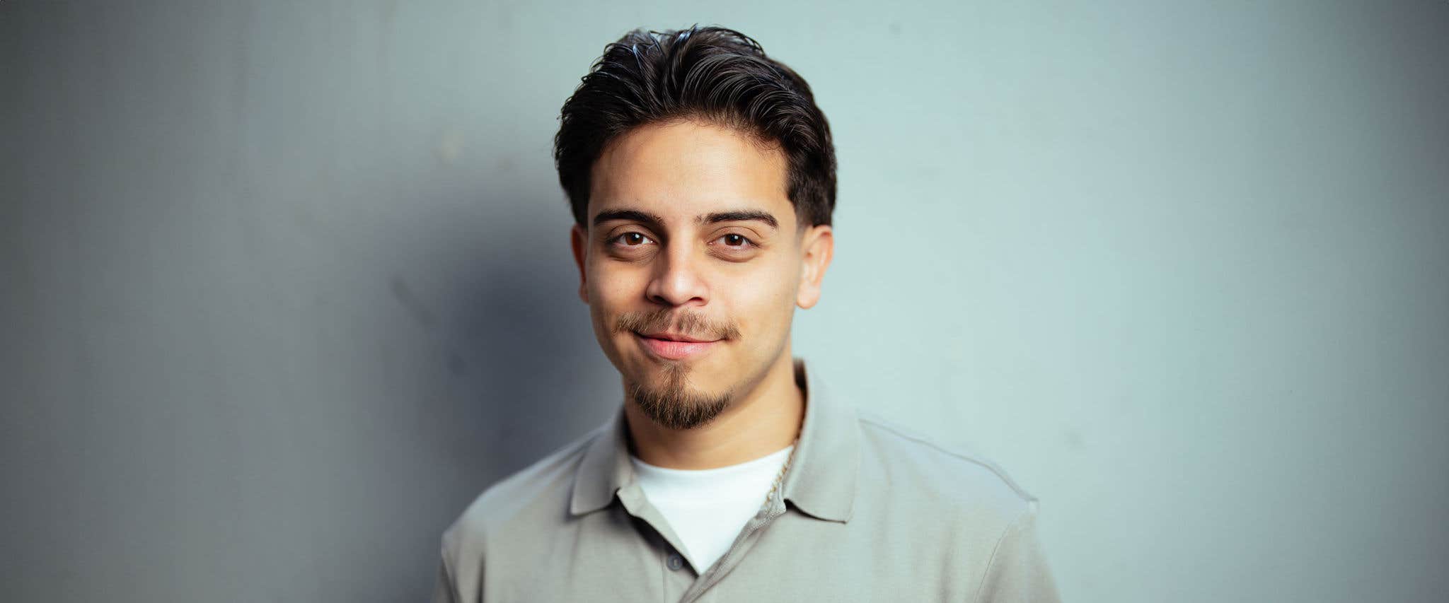 Ralph Barbosa with short dark hair and a light gray shirt smiles in front of a light blue background.