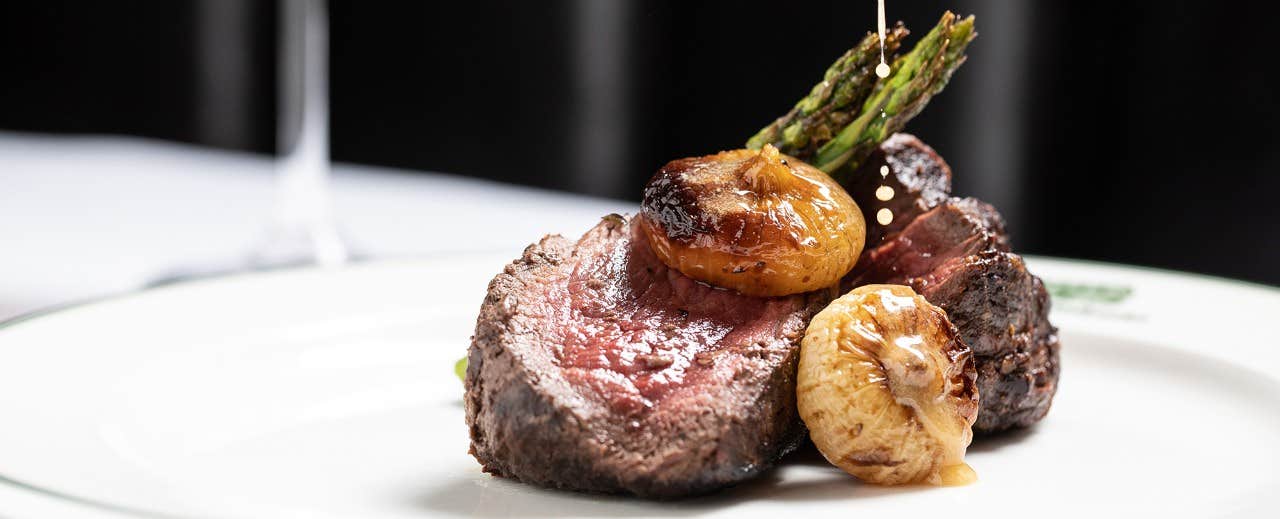 A gourmet steak dish with roasted garlic and asparagus, served on a white plate.