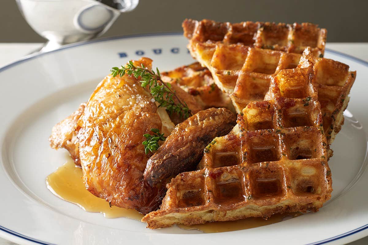 A plate with crispy fried chicken, golden brown waffles, and a drizzle of syrup, garnished with herbs.