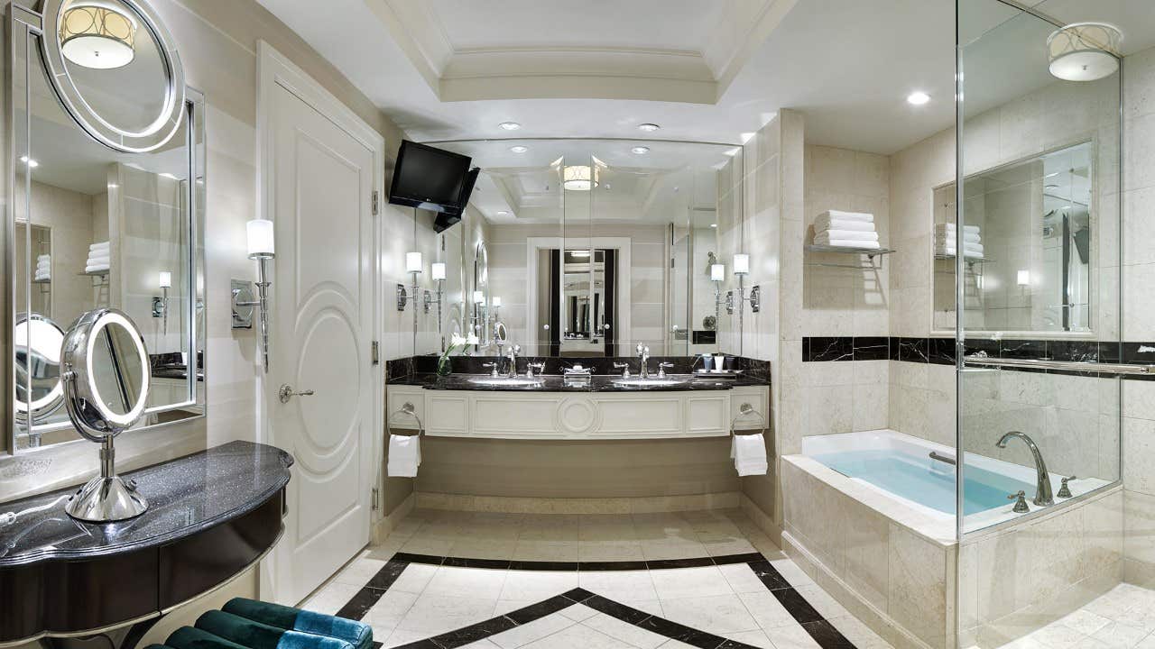 Luxurious bathroom with double sinks, mirrors, bathtub, TV, and modern fixtures in a spacious, elegant setting.