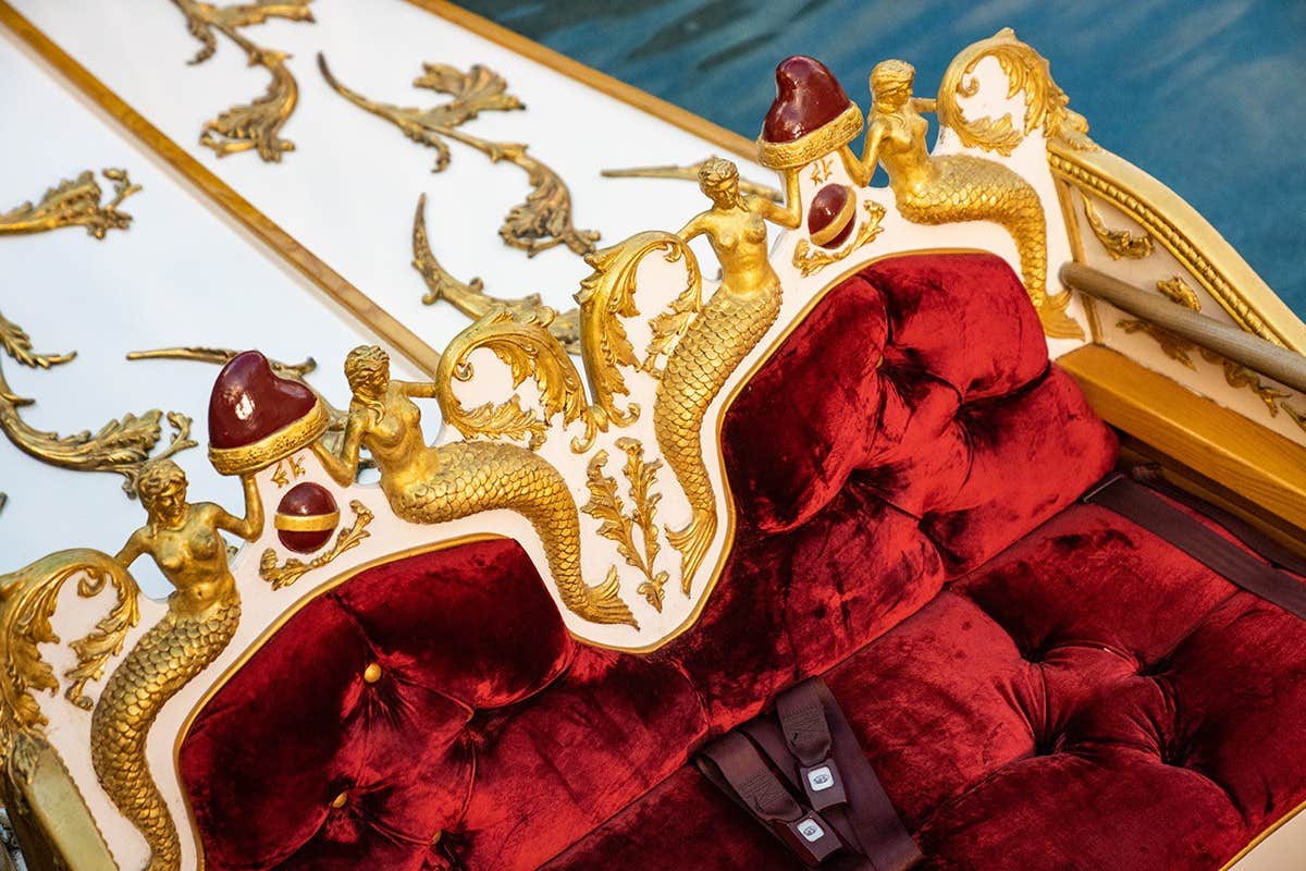 Ornate red velvet seat with gold mermaid carvings and intricate designs on a wooden structure.