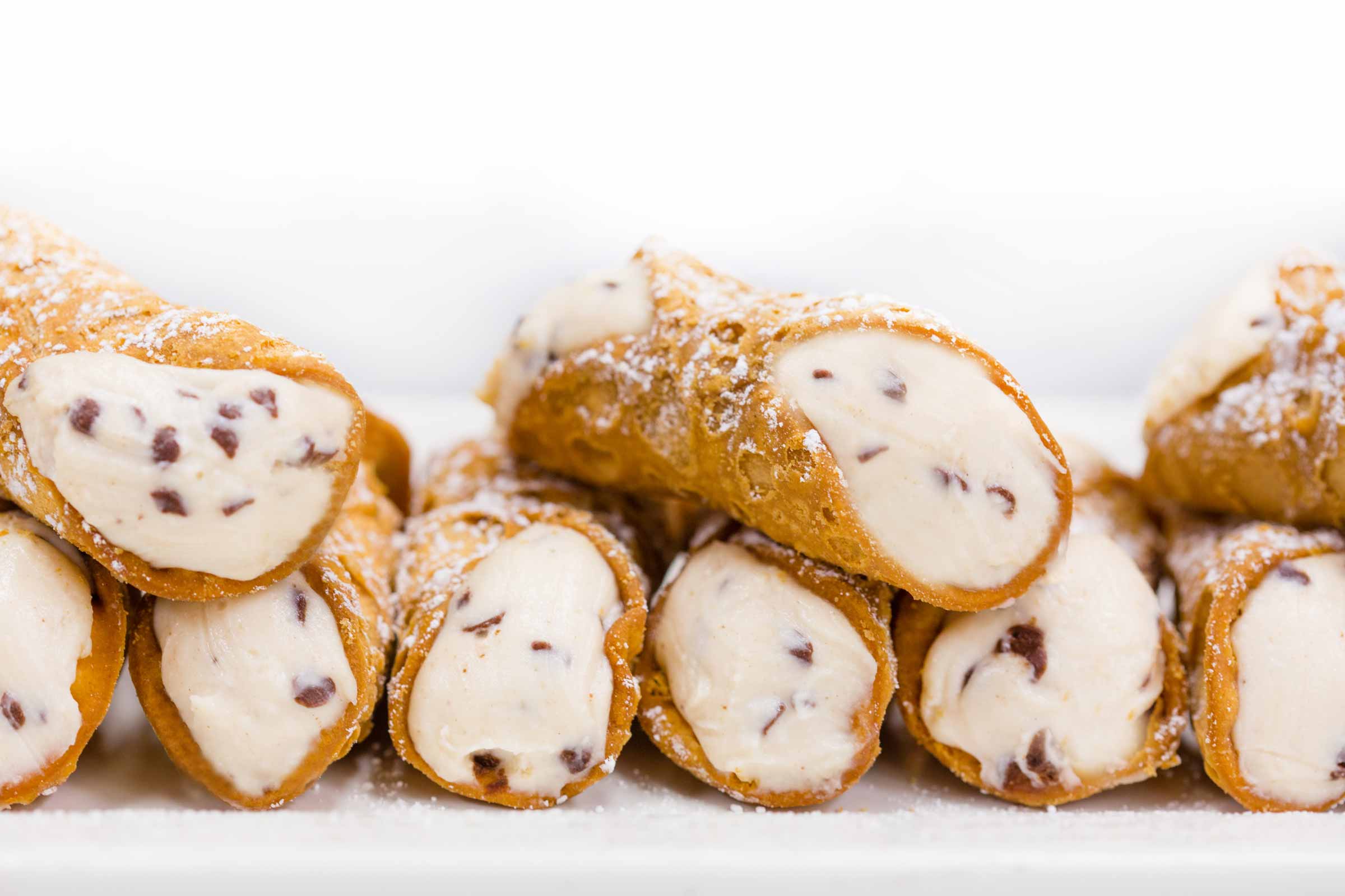 Close-up of a stack of cannoli, filled with cream and sprinkled with powdered sugar.